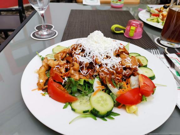 Auf einem glatten Tisch, steht ein flacher Teller mit Nudeln Bolognese und dazu Gemüse.