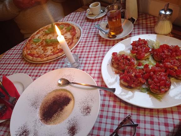 Auf einem Tisch mit weiß-roter Tischdecke, stehen drei Speiseteller, eine Kerze, und Getränkegläser.