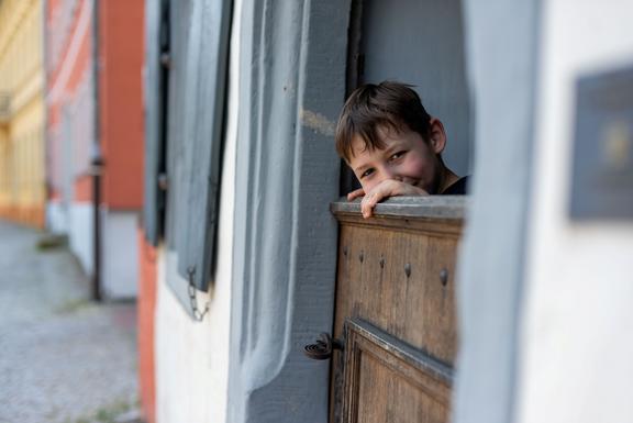 Ein Junge schaut neugierig aus einem historischen Fenster.