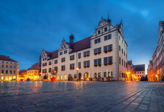 Historisches Rathausgebäude mit Giebeln und vielen Fenstern am abendlichen Marktplatz unter dunklem Himmel, beleuchtet von Straßenlaternen