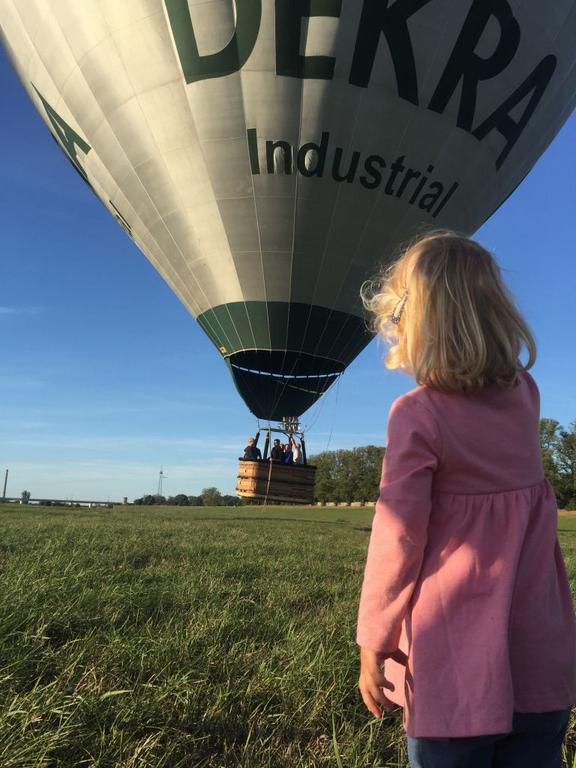 Mädchen in rosa Jacke vor Heissluftballon auf Wiese 