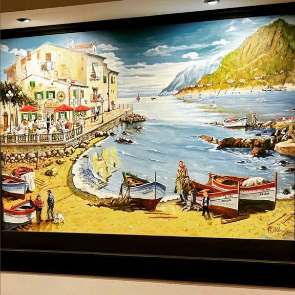 Ein Gemälde, aus dem Dolce Vita mit schwarzem Rahmen, auf diesem Gemälde ist ein Strand, Meer, Stadt, Berge, Personen und ein bewölkter Blauer Himmel zu sehen. 
