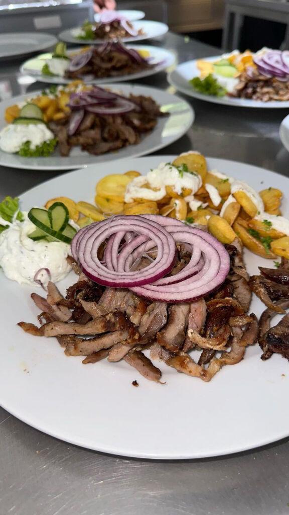 Griechisches Essen mit Gyros, Zwiebeln, Pommes und Zitronenscheiben auf weißem Teller