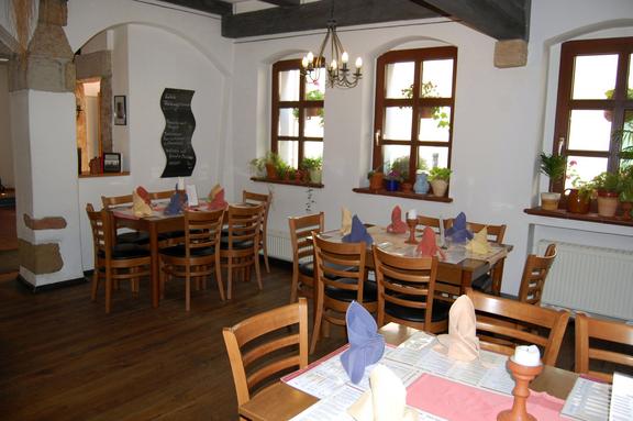 Gastraum Herr Käthe, bestehend aus drei Sitzmöglichkeiten gedeckter Tisch mit Stühlen, weißer Wand drei Fenster mit Holzrahmen.