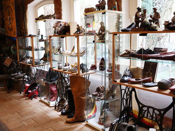 Vitrinen mit historischen Schuhen und Stiefeln in einem Museum mit großen Fenstern und Holzboden