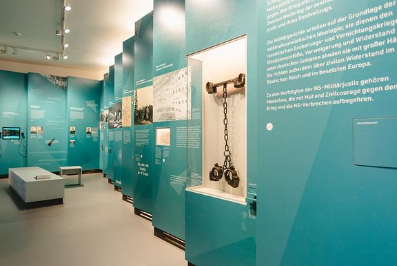 In dem Gebäude, des Erinnerungsortes Torgau, befindet sich eine Ausstellung, mit türkiesen Wänden, weißer Schrift, sowie einem Gang mit Sitzmöglichkeit. 